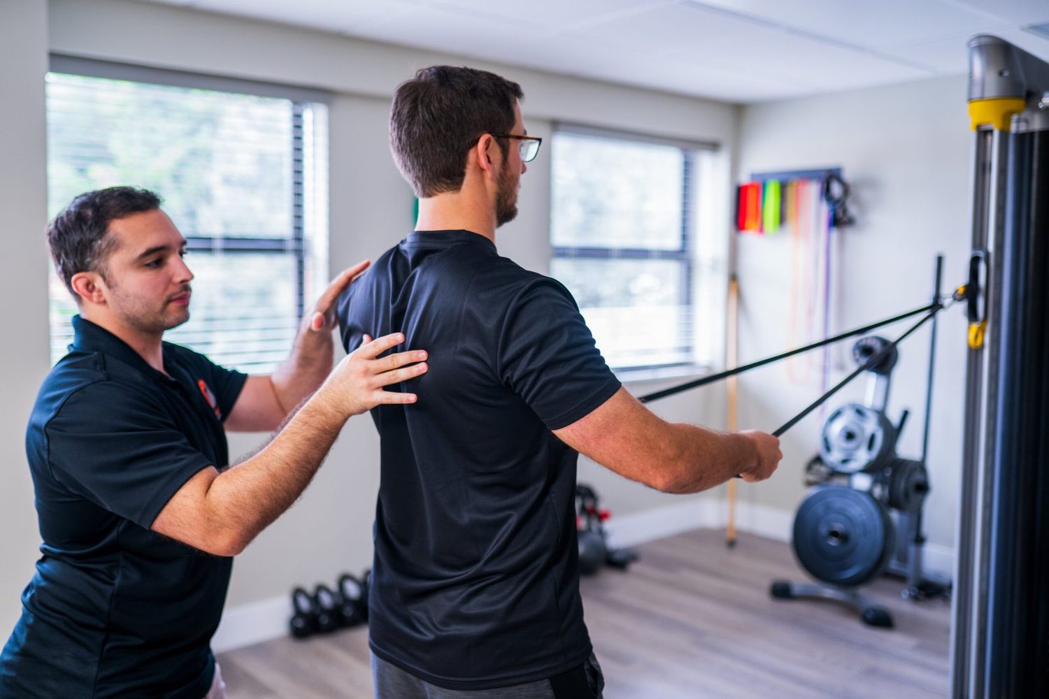 An athlete drawing a cable across the body while a clinician steadies the shoulder blade.