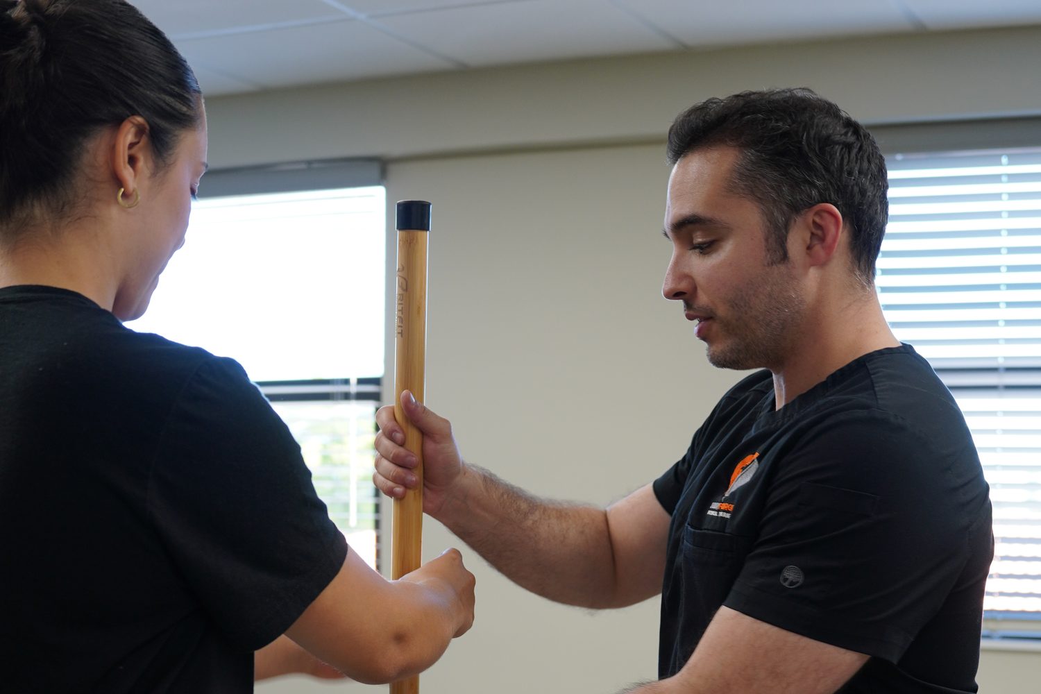 A clinician holding a dowel against an athlete's spine to read overhead position during a movement screen.