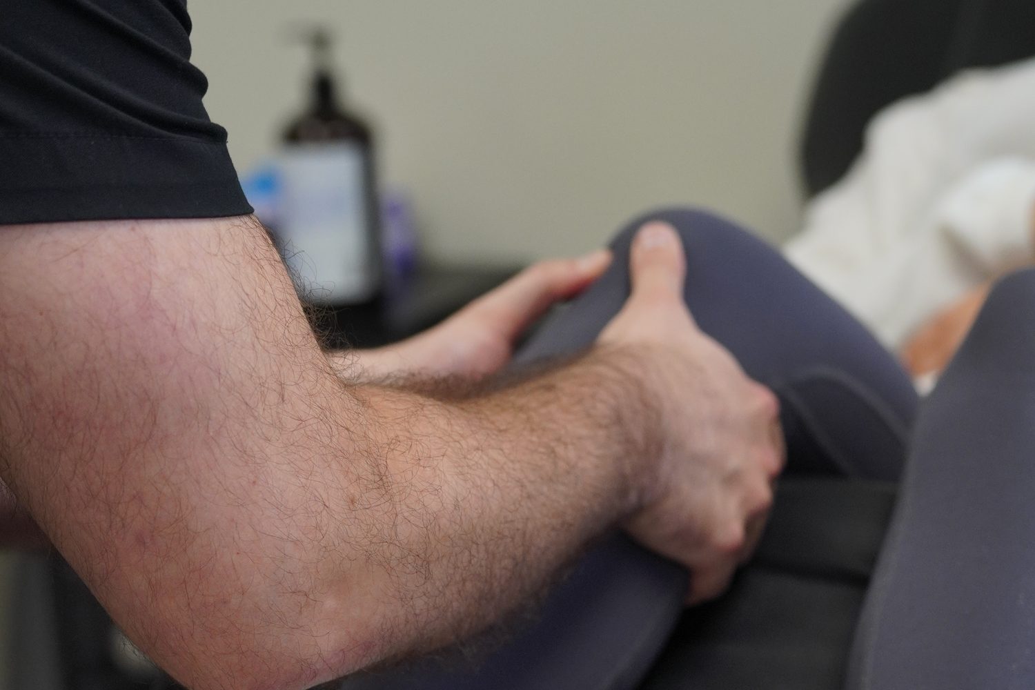 A clinician's hands working along the side of a patient's knee during a recovery session.