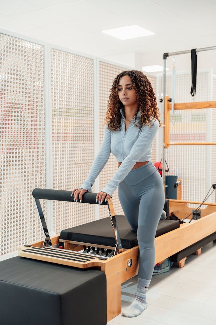Woman practicing Pilates on a reformer machine in fitness studio.